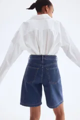 Bermuda de denim azul de tiro alto, corte ancho y largo a la rodilla. Cuenta con cinco bolsillos, cierre frontal con botón y trabillas para cinturón.