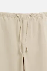 Pantalón de hombre color beige, corte carrot fit, con cintura elástica ajustable con cordón, bolsillos frontales y bolsillo trasero de plastrón.