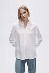 Camisa blanca de manga larga con cuello clásico y cierre frontal con botones. Corte recto y holgado.