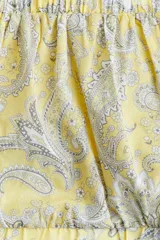 Blusa cropped de algodón color amarillo con estampado paisley en tonos grises. Tiene escote cuadrado elástico, mangas cortas con puños ajustados, espalda descubierta y tiras para atar.