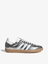 Zapatillas Adidas Samba OG W plateadas metalizadas con efecto craquelado, las tres tiras laterales blancas y suela de goma color caramelo.
