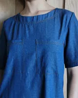 Vestido midi negro con cuello redondo y mangas cortas. Presenta dos bolsillos cuadrados en el pecho y ribetes blancos en cuello, mangas, bolsillos y ruedo.