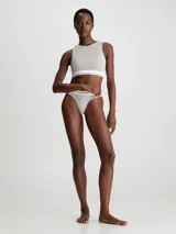 Conjunto Calvin Klein Modern Cotton color gris melange, compuesto por un corpiño deportivo sin mangas y una bombacha tipo tanga, ambos con banda elástica blanca con logo de la marca.