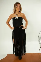 Cinto de cuero negro con flecos largos y hebilla metálica ajustable. Presenta detalles de tachas y argollas metálicas.