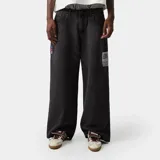 Pantalón de denim negro lavado, corte ancho (loose fit) y tiro alto, con etiqueta rectangular estampada en el muslo derecho y detalle de cinta con colores en el bolsillo delantero izquierdo.