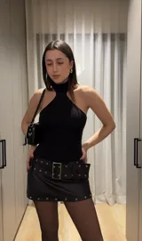 Minifalda negra de cuerina con cinturón con hebillas metálicas.