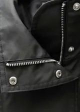Anorak negro oversize con cuello alto, cierre frontal con botones y cremallera oculta, mangas largas con puños abotonados y bolsillos laterales con cremallera.