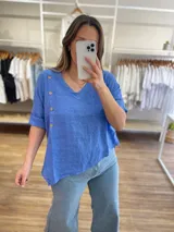 Blusa celeste de lino con cuello en V, mangas cortas con dobladillo y cierre lateral con botones de madera.