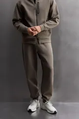 Pantalón jogger color marrón oscuro, corte regular fit, confeccionado en tejido técnico compacto de algodón con elasticidad. Cuenta con cintura elástica ajustable con cordón, bolsillos frontales y bolsillo lateral con cierre de cremallera.