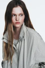 Chaqueta corta de nylon con cuello alto, manga larga y bajo ajustable con cordones. Presenta un estampado de cuadros pequeños en tonos claros.