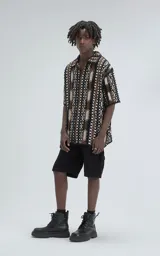 Camisa de manga corta tejida en punto abierto (símil crochet), con calce oversize. Presenta un patrón geométrico en tonos negro, marrón y blanco.