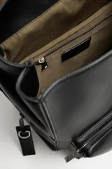 Mochila negra de cuero sintético con solapa y cierre magnético. Tiene un compartimento principal con espacio para dispositivos electrónicos de hasta 13 pulgadas y un bolsillo con cierre. En la parte frontal tiene un bolsillo con cierre y bolsillos planos en los laterales. La parte posterior es acolchada y tiene una banda de sujeción para equipaje. Tiene asa de mano y dos asas de hombro ajustables y acolchadas.