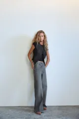 Pantalón de jean celeste de tiro alto, corte wide leg y largo hasta el tobillo. Presenta un diseño asimétrico en la cintura con cierre frontal cruzado con cremallera y botones metálicos.