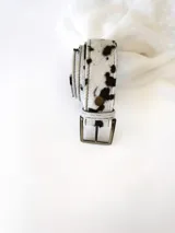 Cinto de cuero con forro de cuero, estampado animal print de vaca en blanco y negro, con hebilla metálica rectangular color bronce y broche suizo.