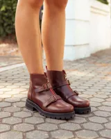 Botinetas de cuero color marrón con suela track negra. Presentan un cierre frontal con detalle en color rojo, dos correas con hebillas metálicas ajustables y puntera redondeada.