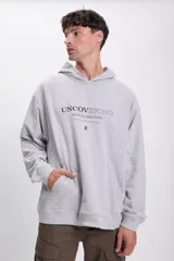Canguro deportivo gris claro con capucha y bolsillo tipo canguro. Estampado frontal con la frase "Uncovering revealing hidden truths" y un pequeño logo.