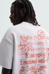 Sudadera lila de corte holgado con cuello redondo y manga corta. Presenta textos estampados en color rojo en el frente y la espalda. Tiene efecto lavado y acabados irregulares.