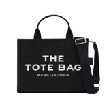 Bolso tote mediano de lona color negro con asas superiores y correa tejida ajustable y desmontable. Presenta estampado frontal en blanco con el texto "THE TOTE BAG" y "MARC JACOBS". Incluye cierre de cremallera.