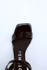 Sandalias de cuero charol negro con tira delgada sobre los dedos, pulsera con hebilla al tobillo y tacón cuadrado.