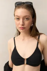 Top de bikini negro con textura sutil y aro rectangular dorado en el centro. Breteles finos y espalda con cierre de gancho.