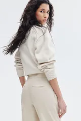 Pantalón cigarette color beige de tiro alto, con cierre y corchetes ocultos, bolsillos laterales discretos y bolsillos insertados decorativos atrás. Piernas ajustadas con abertura en los bajos y pliegues adelante y atrás.