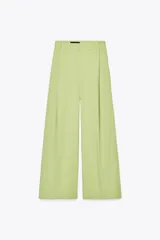 Pantalón verde claro de tiro alto con trabillas y botón en la cintura. Tiene pliegues, bolsillos laterales y falsos bolsillos de vivo en la espalda. El cierre frontal es con cremallera, botón interior y ganchos metálicos.