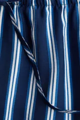 Pantalón de corte holgado en sarga con estampado a rayas verticales azules y blancas. Modelo de talle alto con cintura elástica y cordón de ajuste fino.
