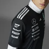 Camiseta negra de manga corta con cuello redondo, con logos de Mercedes AMG Petronas F1 Team y sponsors estampados en el frente y las mangas. Presenta las tres rayas blancas de Adidas en los hombros.