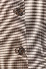 Chaleco marrón claro con estampado de cuadros, cuello redondo, sin mangas y cierre frontal con botones marrones.