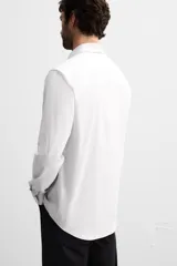 Camisa celeste de corte slim fit, confeccionada en tejido de algodón. Tiene cuello italiano, mangas largas con puños abotonados y cierre frontal con botones.