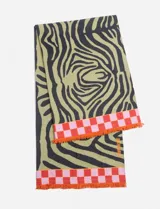 Pareo rectangular de algodón con estampado abstracto en negro y verde sobre fondo blanco. Tiene flecos en los extremos y un borde a cuadros rojos y rosas.