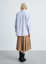Camisa celeste y blanca a rayas verticales, de corte recto y mangas largas con puños abotonados.