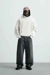 Sudadera con capucha color crudo, de corte relajado, confeccionada en tejido de algodón con interior rizado. Cuenta con cuello con capucha, manga larga, bolsillo frontal tipo canguro y acabados en rib.