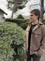 Camisa marrón de lana con corte clásico, cuello camisero, cierre frontal con botones, dos bolsillos de parche con solapa abotonada en el pecho y puños abotonados. Presenta un pequeño logo bordado en uno de los bolsillos.