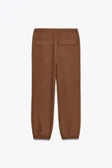 Pantalón jogger color gris claro, de tiro alto con cintura elástica ajustable con cordones, bolsillos delanteros y traseros con solapa, y puños elásticos en el bajo.