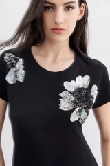 Remera negra de algodón con calce relajado, cuello redondo y mangas cortas. Presenta bordados florales con lentejuelas en el frente.