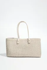 Bolso shopper alargado color beige con diseño trenzado, doble asa de hombro y cierre con botón imantado. Incluye bolsa interior con cierre fruncido.