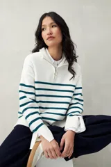 Polera blanca de punto con cuello alto y cierre metálico, de calce relajado y diseño a rayas horizontales azules.