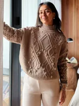 Sweater tejido grueso color rosa, con cuello alto, mangas largas y diseño trenzado con detalles de pompones.