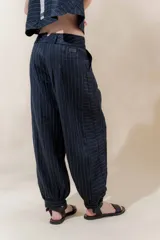 Pantalón de lino color marrón, con corte tipo barrel, tiro medio, pretina ancha con doble abotonadura, bolsillos laterales y pinzas en el frente. Ruedo con presilla permitiendo usarlo recto o fruncido al tobillo.