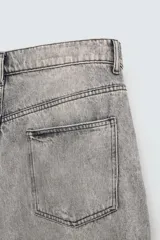 Pantalón de jean gris con lavado gastado, corte holgado, tiro medio, cinco bolsillos y roturas. Cierre frontal con cremallera y botón.