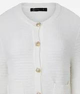 Cardigan de punto blanco, con cuello redondo, manga larga y cierre frontal de botones dorados. Posee dos bolsillos cuadrados en la parte delantera inferior.
