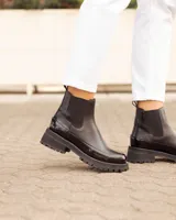 Botas Chelsea negras de cuero, con suela track y detalles de charol en la puntera y el talón.