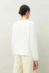 Camisa celeste de corte holgado con botones frontales, canesú con tablas y mangas 3/4 amplias con puño elastizado.