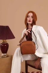 Bandolera de cuero sintético color beige, con diseño compacto y elegante. Cuenta con un bolsillo frontal con cierre y un compartimento principal con cierre. La correa es regulable.