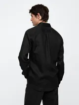 Camisa de lino para hombre en color beige, de manga larga con cuello clásico y cierre frontal de botones. Presenta un bolsillo de parche en el pecho con el icónico logo del oso Brannan bordado.