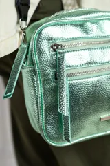 Cartera bandolera rectangular color verde metalizado con tres cierres frontales y correa de tela negra regulable.