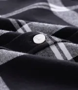 Camisa de franela para hombre con estampado de cuadros en blanco y negro. Tiene cuello inglés, mangas largas, bolsillos en el pecho y abotonado delantero.