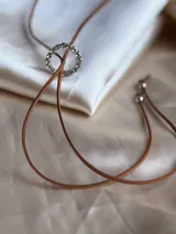 Gargantilla marrón de cuero sintético con dije circular con strass y lazos para atar.