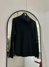 Sweater negro de cuello alto envolvente con detalle tejido en espiga en el centro.